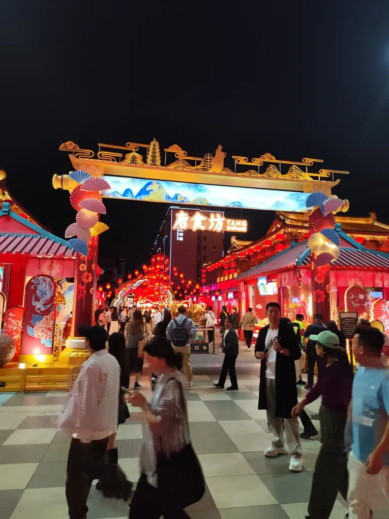 Calle comercial nocturna en China con un arco tradicional iluminado y faroles rojos.