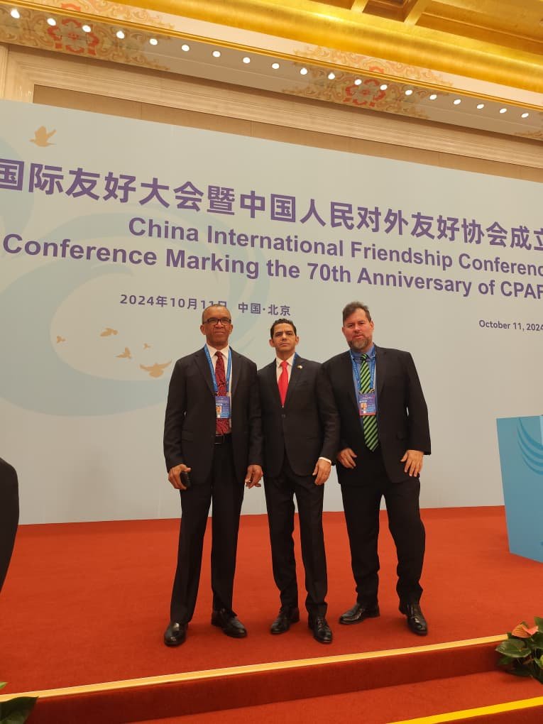 Tres delegados de AVEACHI posan ante el panel oficial de la Conferencia Internacional de Amistad de China por el 70 aniversario de la CPAFFC en Beijing, octubre de 2024.